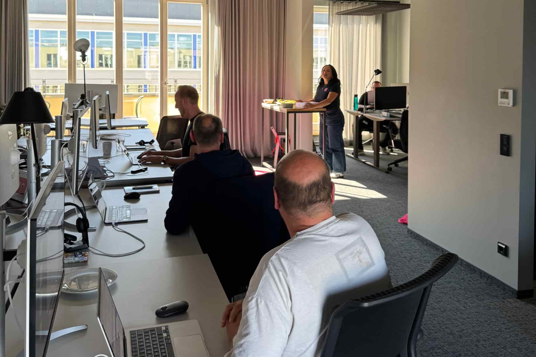Mitarbeiter schauen von ihrem Arbeitsplatz zu einer Person, die redet.